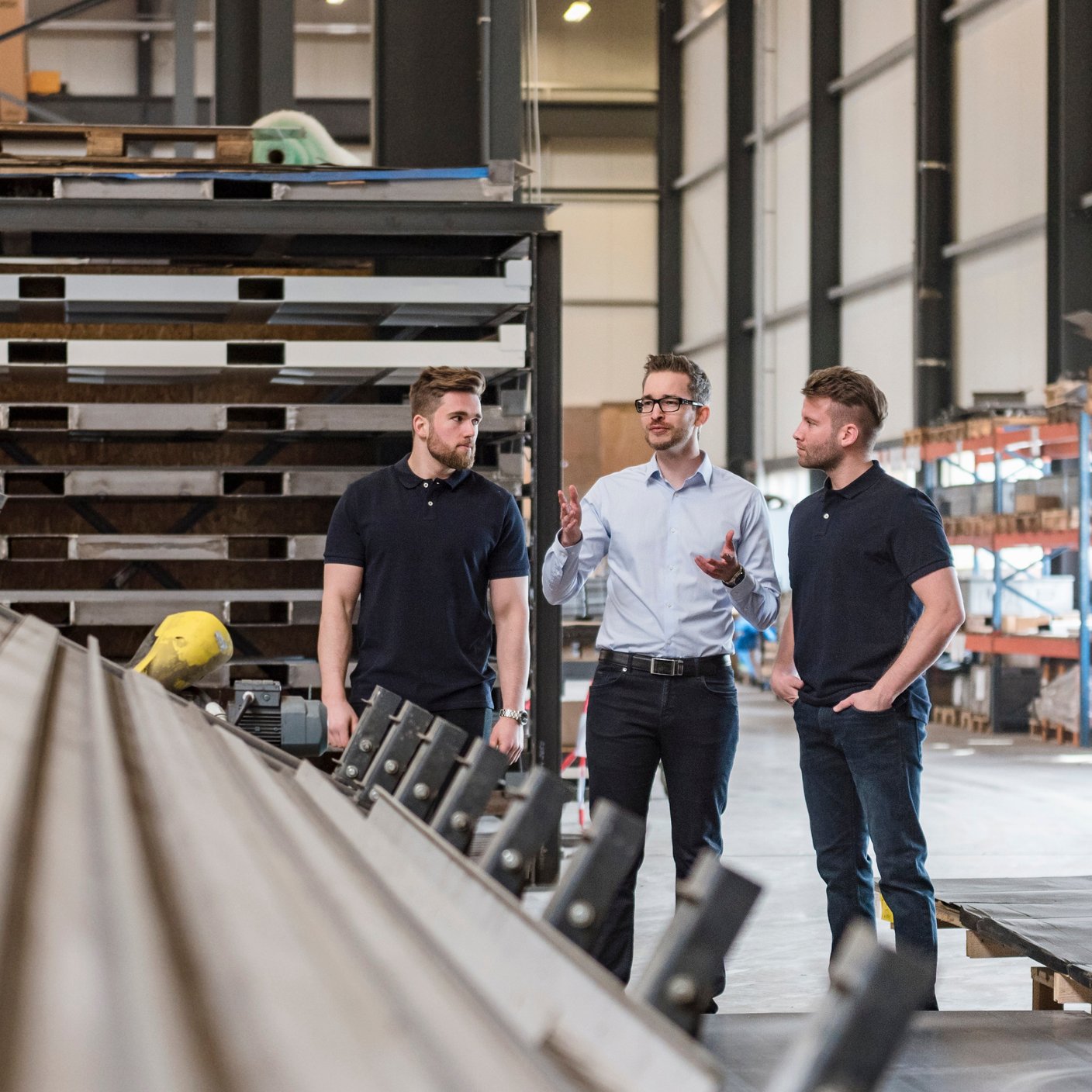 Three men talking on factory shop floor.