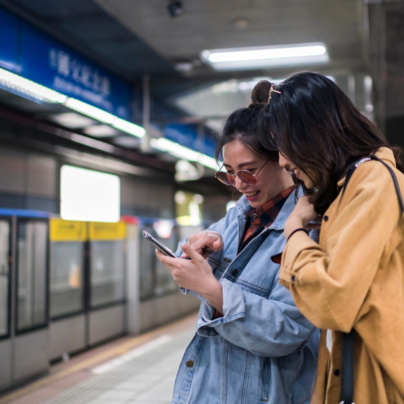 Des femmes préparent leur voyage sur leur téléphone portable, en attendant dans une station de métro.