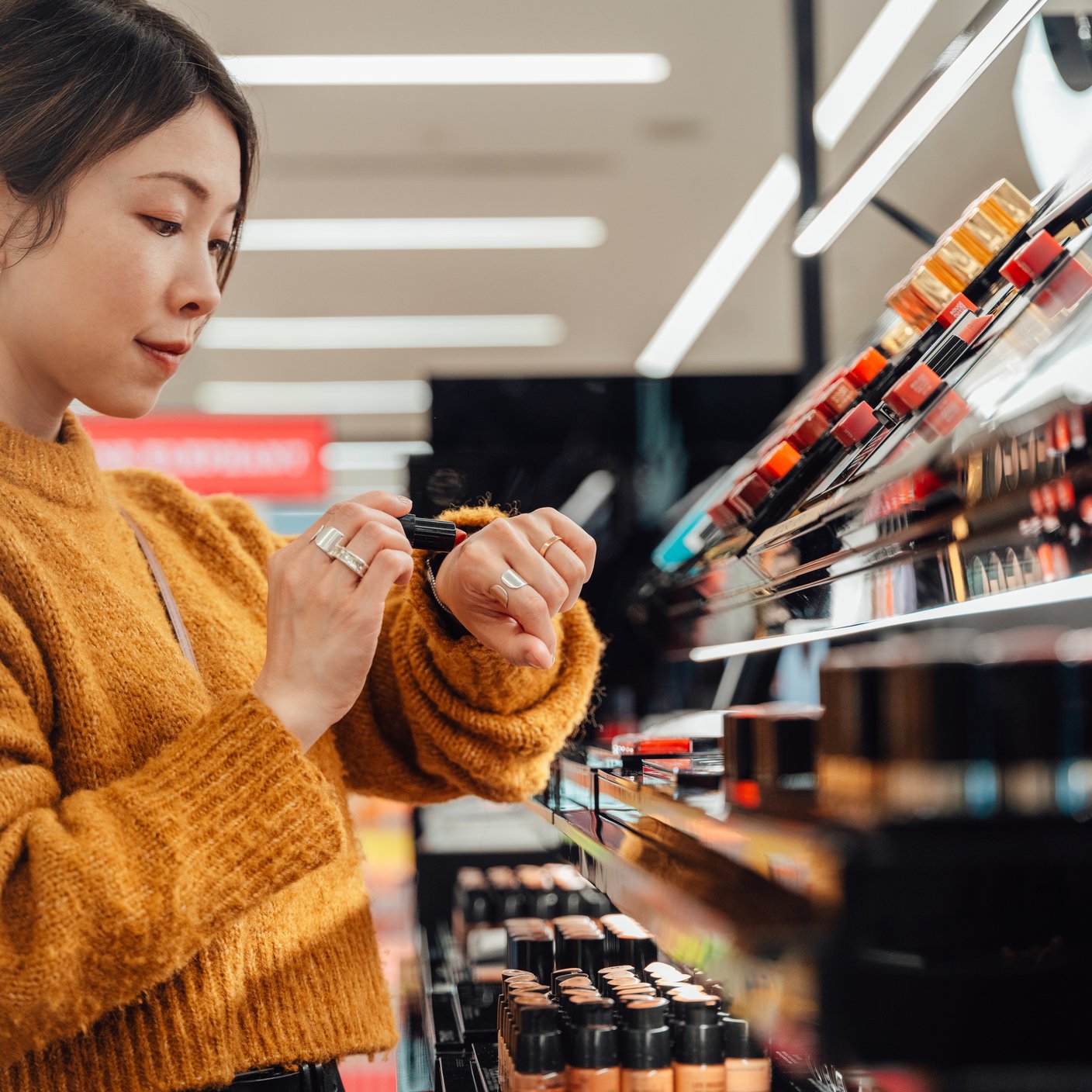 Young woman picking lipstick shades at cosmetics counter.