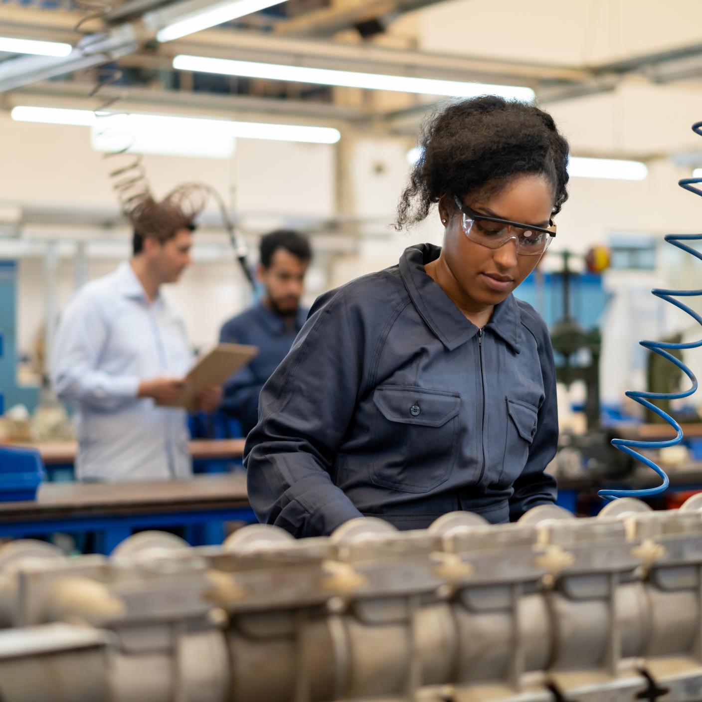 Afro-Amerikaanse jonge vrouw aan het werk bij een assemblageproductie van waterpompen in een fabriek - incidentele mensen op achtergrond