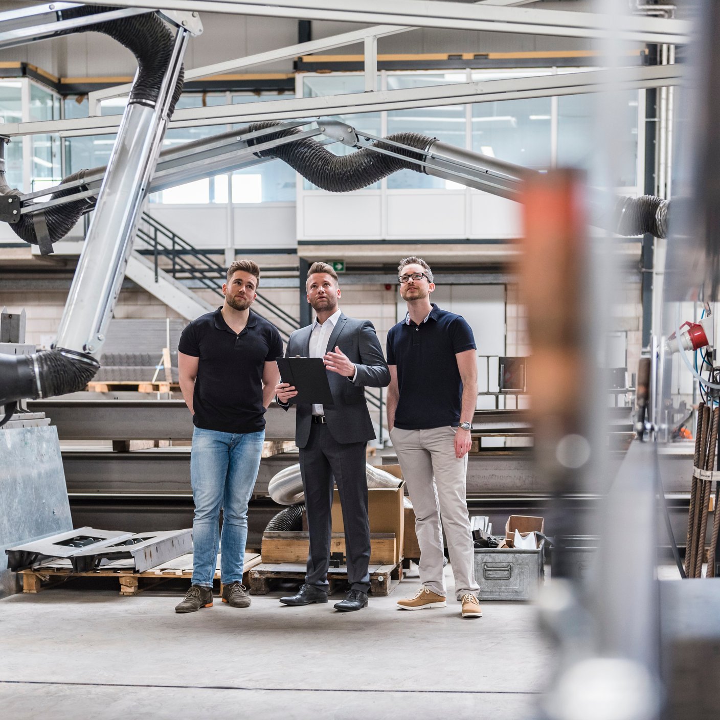 Three men talking on factory shop floor.