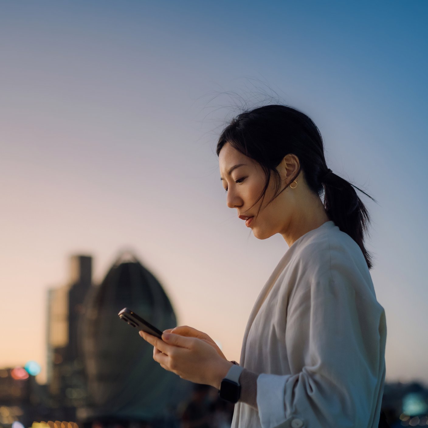 Modern young Asian woman walking in the city text messaging on smartphone on the go.