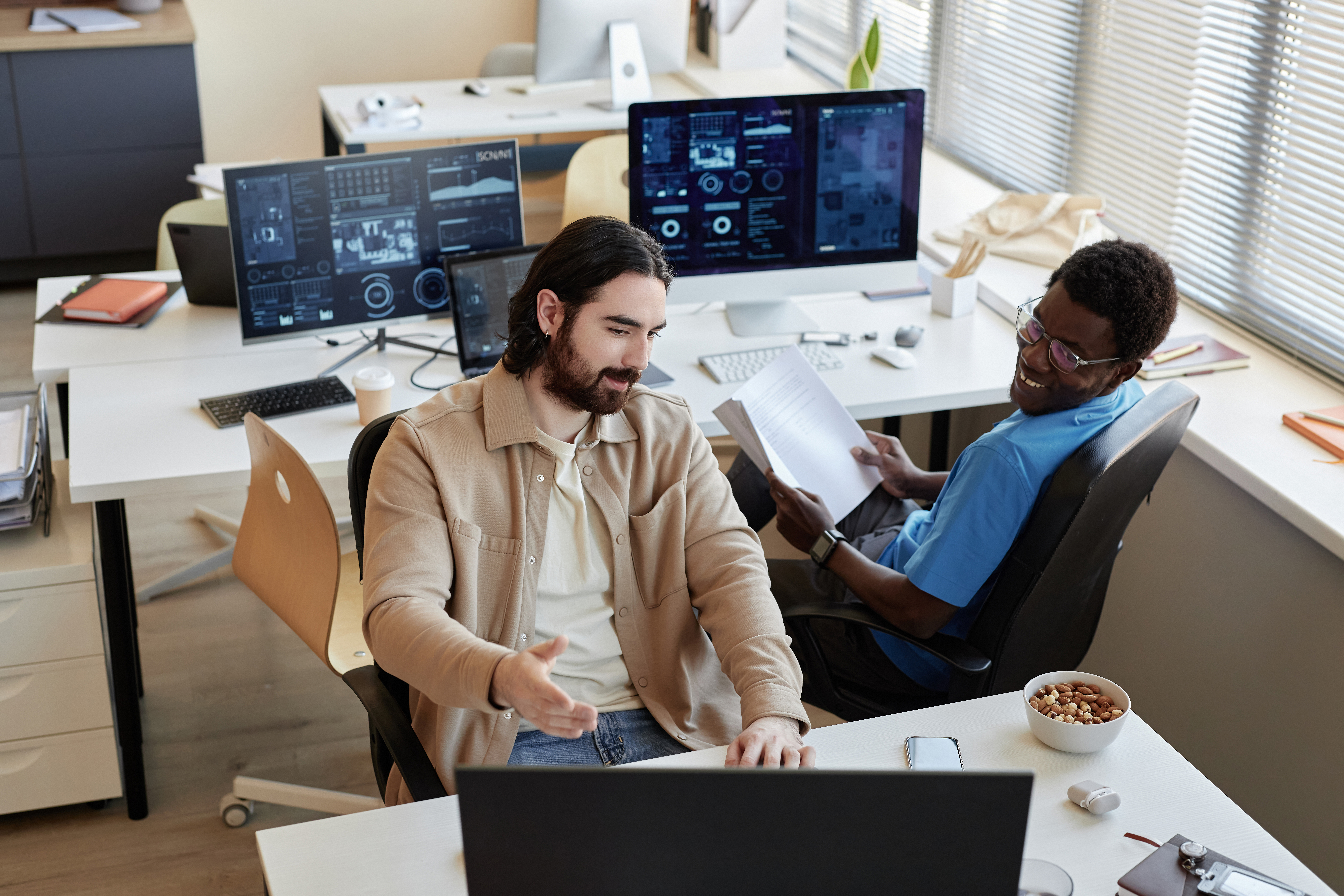 Young businessman showing data on computer screen to smiling colleague while explaining him results of analyzing it.