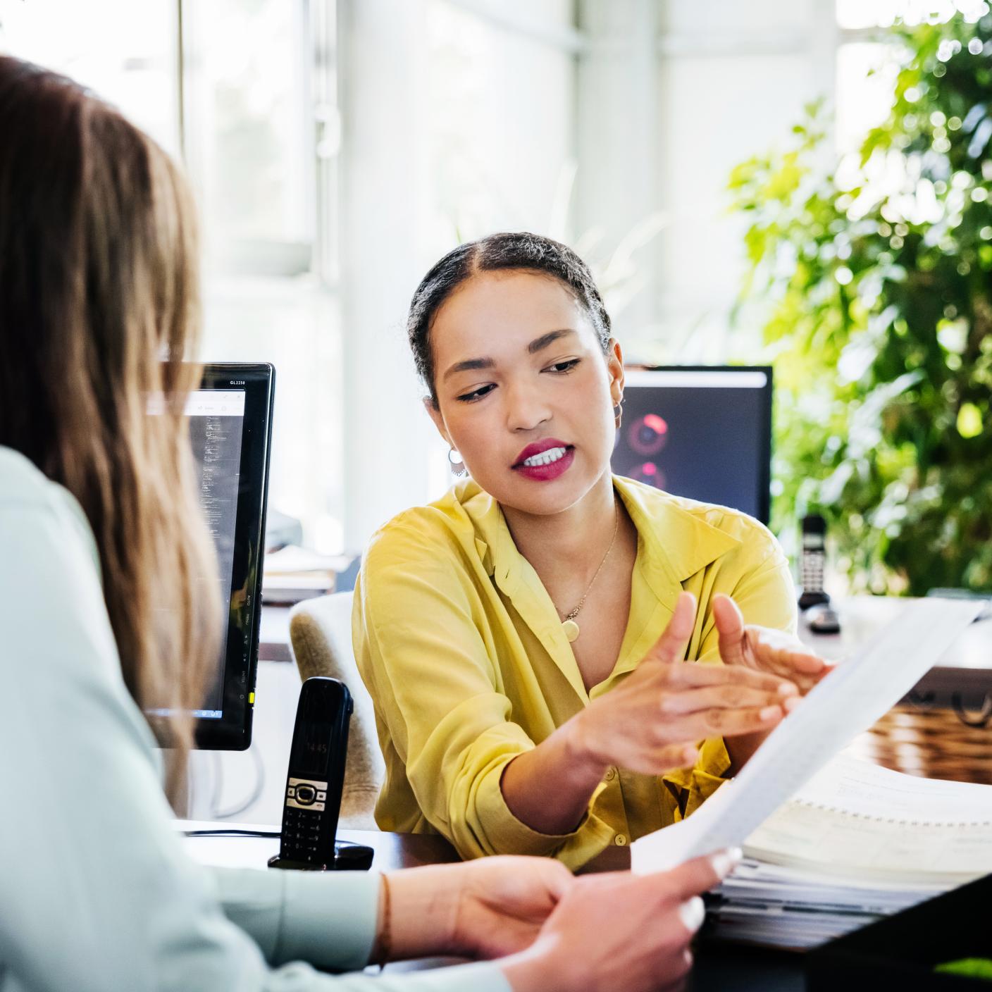 A person looking at some paperwork with one of her colleagues in a modern and fresh office environment.